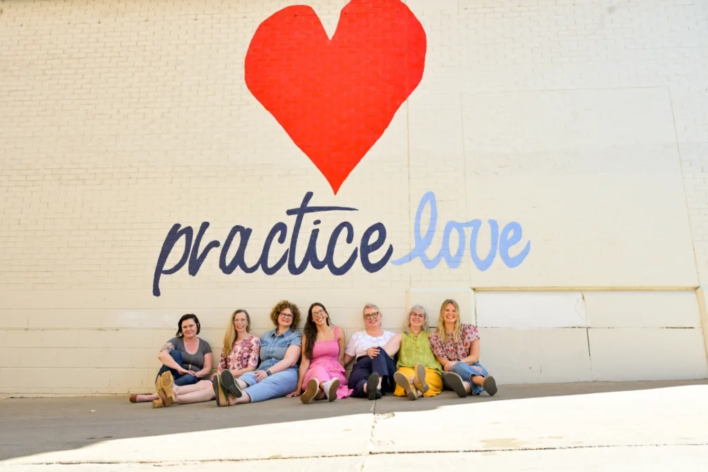 A Group of Women under a large heart and painting that says practice love