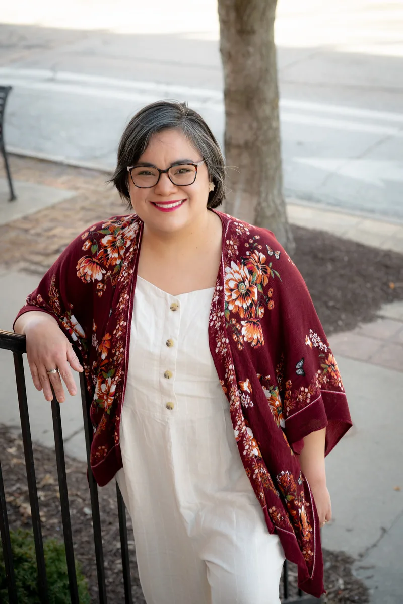 Alyssa Palante smiling outdoors wearing a floral maroon kimono and white buttoned jumpsuit