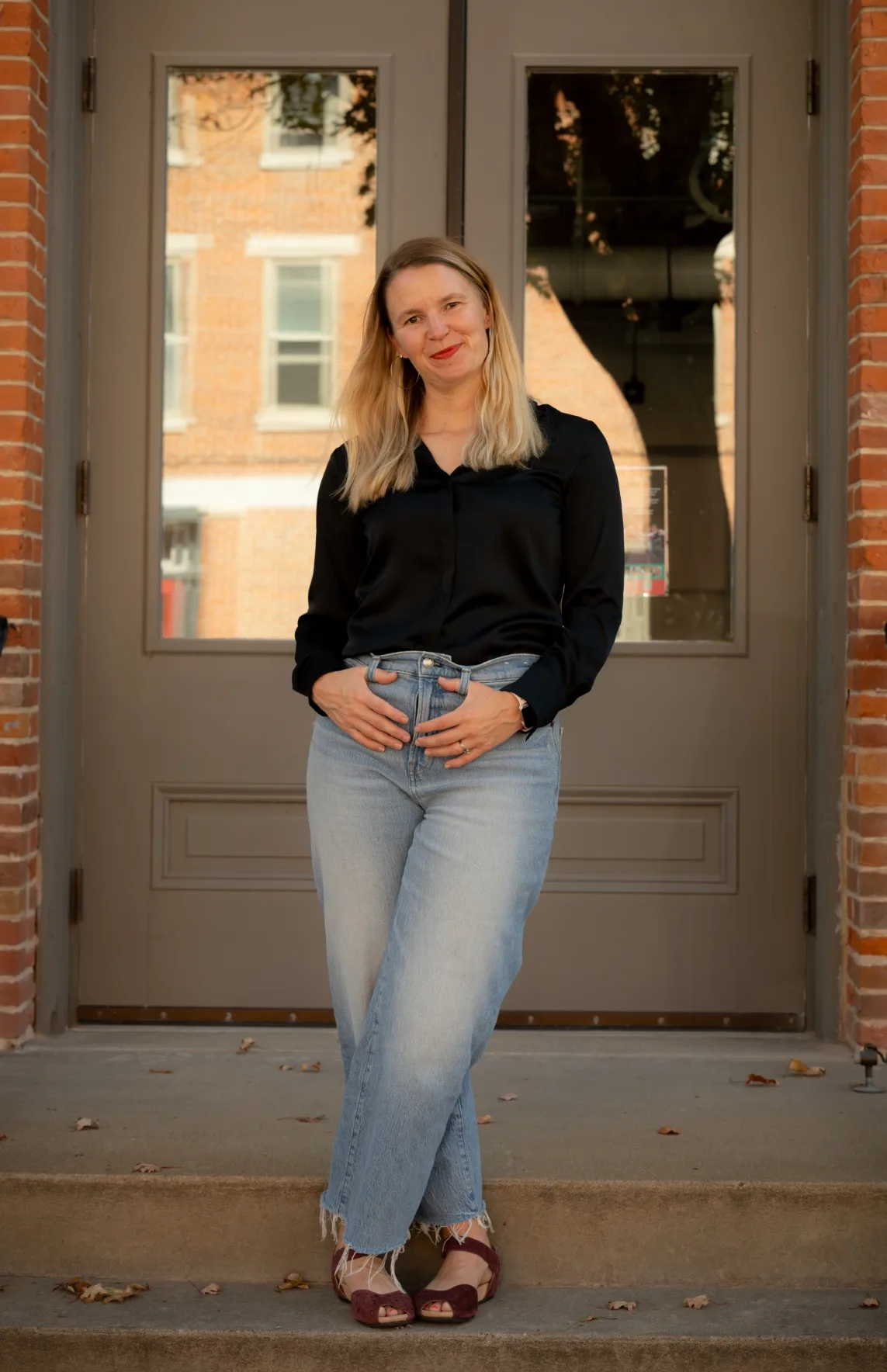 Portrait of therapist Mariah standing on building steps in front of a doorway, smiling confidently.