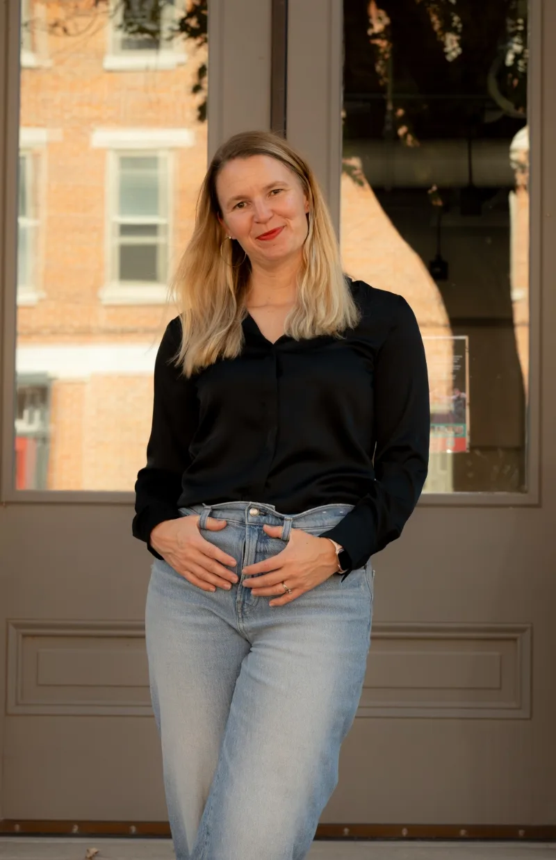 Portrait of therapist Mariah standing on building steps in front of a doorway, smiling confidently.
