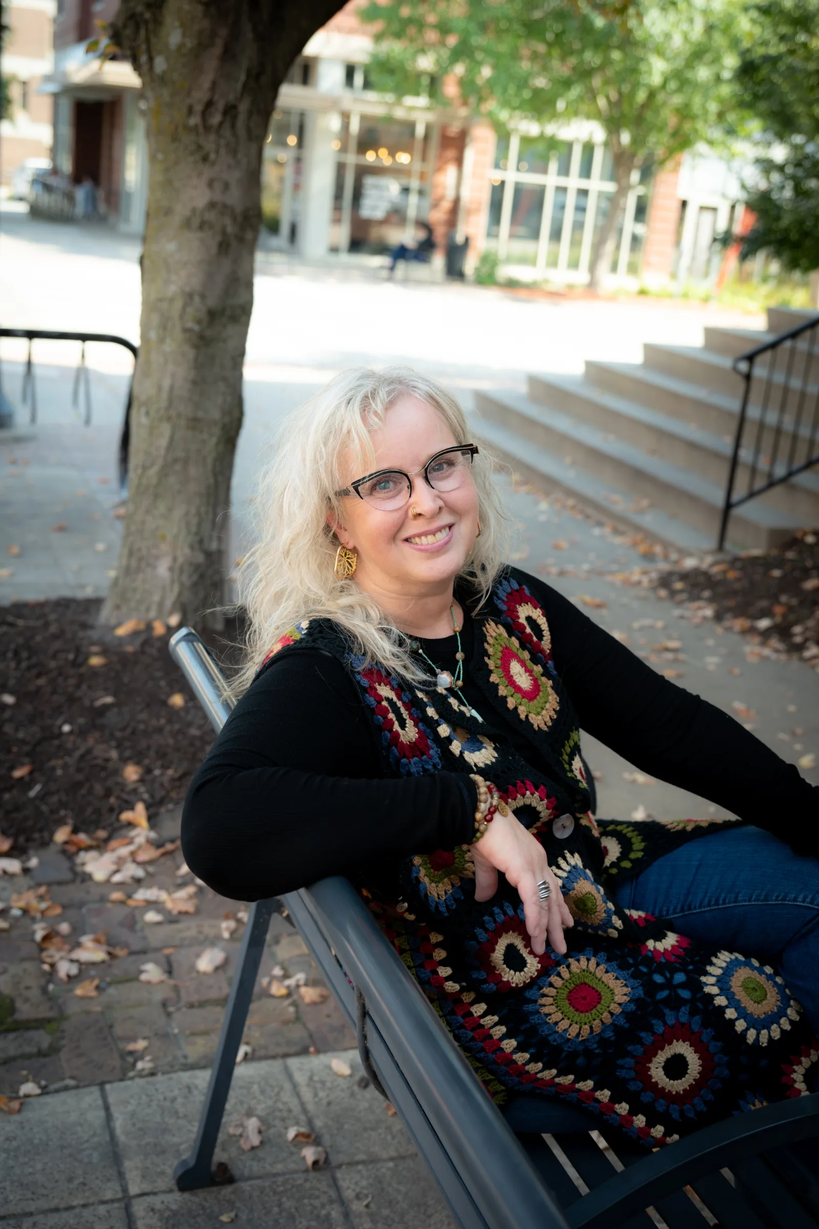 Portrait of therapist Megan sitting on an outdoor bench, smiling and wearing a colorful patterned vest.