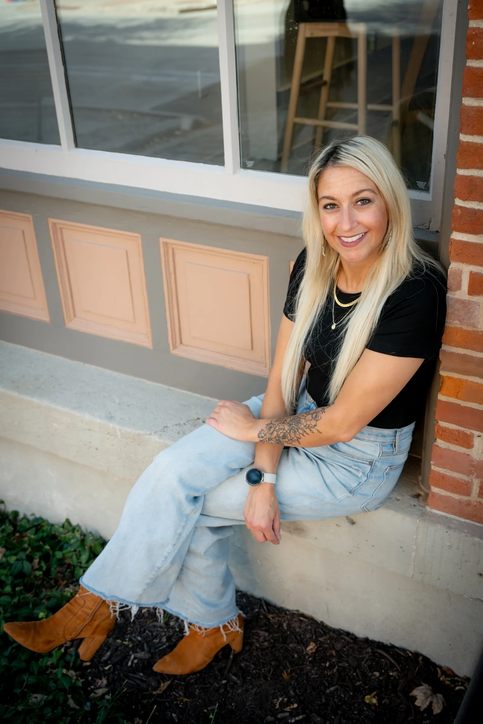 Portrait of therapist Stephanie sitting outside by a window ledge, smiling warmly at the camera.